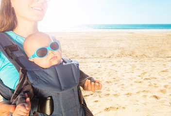 Mother and infant baby in carrier on the sea beach