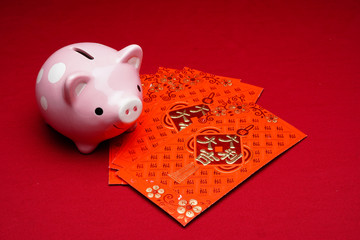 Chinese New Year red envelope with coins and piggy bank in red background. Chinese characters means...
