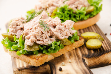 Homemade tuna salad sandwiches on cutting board with pickles aside