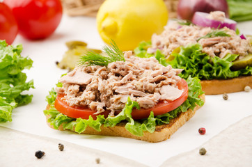 Tuna sandwiches with lettuce tomatoes and onions on parchment paper