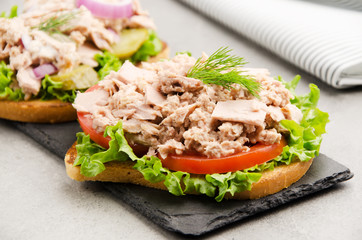 Tuna sandwiches with lettuce tomatoes pickles and onions on slate tray