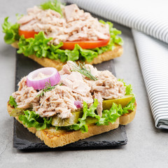 Tuna sandwiches with lettuce tomatoes pickles and onions on slate tray
