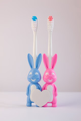 Children's toothbrushes in a form of cute blue and pink bunnies on a white background isolated. Two rabbits with blank heart.Kids oral care, first deciduous teeth hygiene, bathroom supplies, dentistry