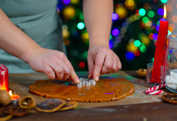 Cook's hands cut out cookie from rolled dough on a Christmas tree background.