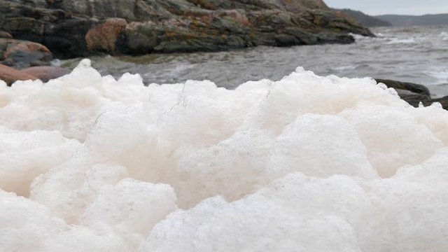 Close view of sea foam jiggling in shoreline waves of a rocky coast