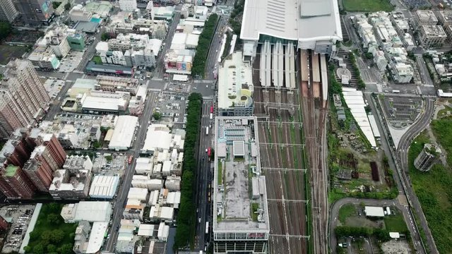 Tilting shot, orange train moving in high speed railways and cars on the highway, tall buildings in the background.