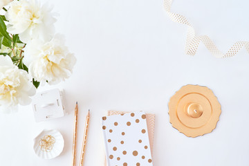 Flat lay blogger or freelancer workspace with a notebook and white peonies in a vase on a white table