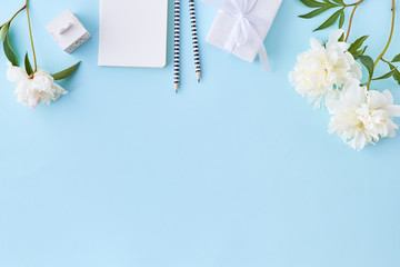 Flat lay blogger or freelancer workspace with a notebook and white peonies on a blue background