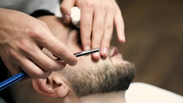 A client has a beard. He has dark hair. A barber is working in salon.