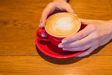 Tasty cappuccino in white cup in street cafeteria on wooden table, female hands holding cup, person having relax and time for dreaming, coffee in great afternoon energy idea.