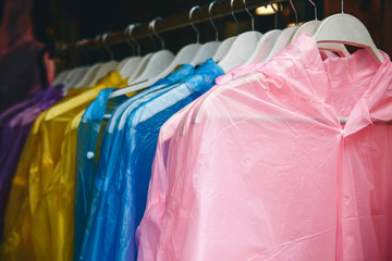 Multi-colored transparent waterproof raincoats hang in a row on a hanger