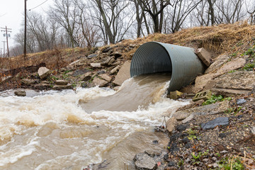 Closeup motion blur of storm water runoff flowing through metal drainage culvert under road....