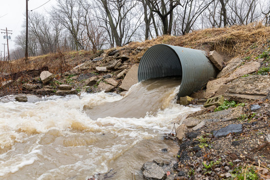 Closeup motion blur of storm water runoff flowing through metal drainage culvert under road. January storms brought heavy rain and flash flooding to Illinois