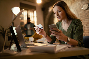 Young businesswoman using credit card and smart phone in the office.