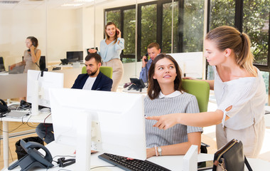 girl helping female colleague in work with computer