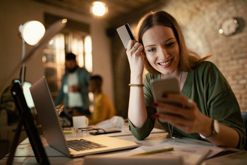 Young happy businesswoman m-banking while working late in the office.