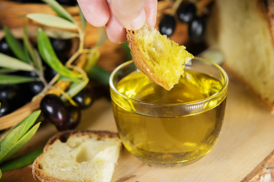 Close up of a glass bowl full of olive oil with bread and olive brunches. healthy fats