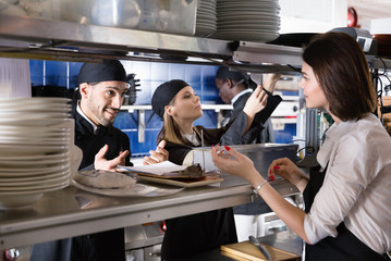 Woman waiter is giving order to chef cook on kitchen in restaurant.