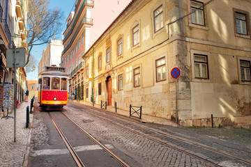 Fototapeta na wymiar The traditional 28 tram passes in a street of the Alfama, Lisbon, Portugal