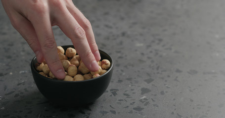 man hand takes hazelnuts from black bowl on terrazzo countertop