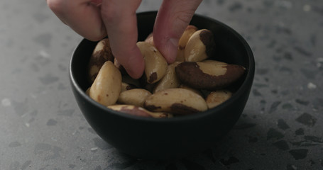 man hand takes brazil nuts from black bowl on terrazzo countertop
