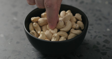 man hand takes cashew nuts from black bowl on terrazzo countertop