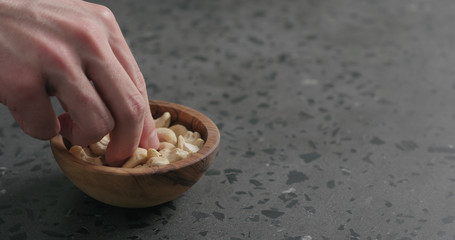 man hand takes cashew nuts from olive bowl on terrazzo countertop