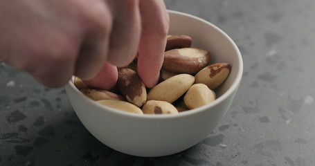 man hand takes brazil nuts from white bowl on terrazzo countertop