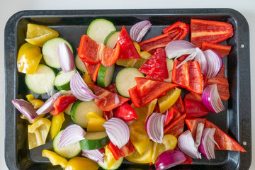 From above shot of prepared raw peppers, onions and courgettes on a roasting tray