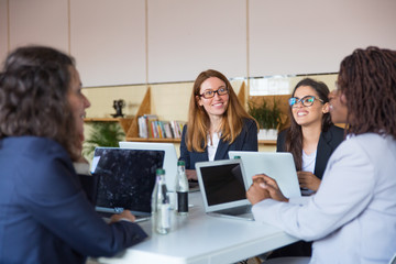 Content businesswomen discussing work in office. Group of professional multi ethnic businesswomen sitting around table and working with laptops in office. Women in business concept