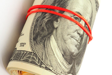 A bundle of old-style 100 dollar bills lies on a white paper background. Banknotes are rolled up...