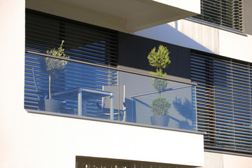 Balkongeländer aus Glas und Edelstahl, dahinter Fenster mit modernen Jalousien