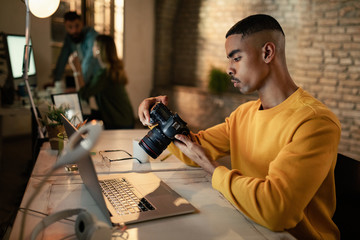 African American photographer looking at images on camera while working late in a studio.