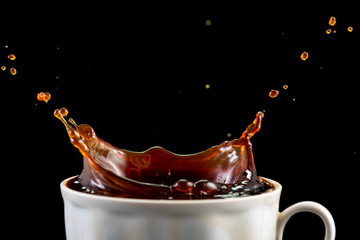 splash and splatter from a piece of sugar in a mug with coffee on a black background