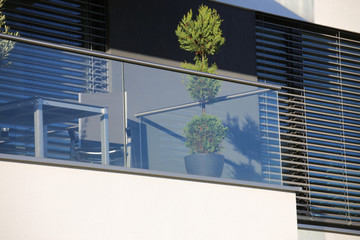Balcony railings made of glass and stainless steel, behind them windows with modern blinds