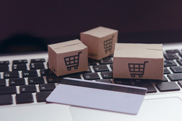 Naklejka na ściany i meble Online shopping - Paper cartons or parcel with a shopping cart logo and credit card on a laptop keyboard. Shopping service on The online web and offers home delivery...
