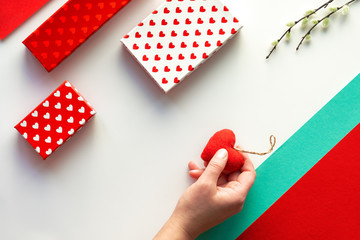 Valentine day flat lay, top view on white. Geometric background with pussy willow. Gift boxes and soft textile toy heart in hand.