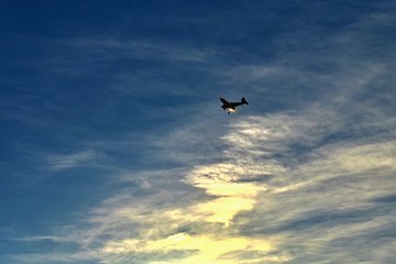 Fototapeta na wymiar Small airplane on blue sky with clouds and sunset in background