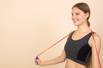 beautiful young woman in sportswear on a beige background with a skipping rope in hands