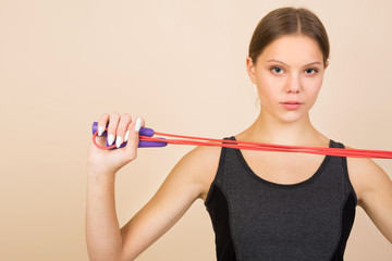 beautiful young woman in sportswear on a beige background with a skipping rope in hands