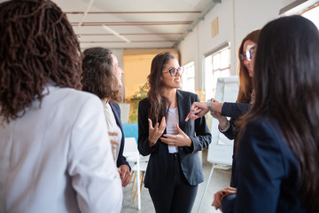 Group of young women standing in circle and discussing project. Smiling creative business team talking in office. Teamwork concept