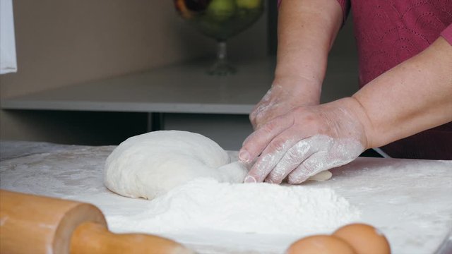 Close-up hands of senior female is cuts a dough into pieces for making ravioli on the table at home kitchen, front view