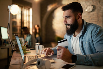 Fototapeta premium Smiling businessman using credit card and laptop for online banking from his office.