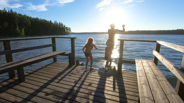 Family couple with daughter running on a wooden pier and jumping into the lake after the sauna in summer white night in Finland.