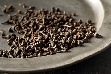 Heap of raw, dried cinnamon blossom buds spice on metal plate on rustic black table