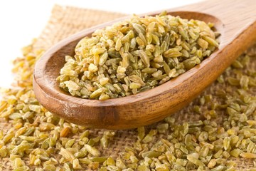 Heap of uncooked, raw freekeh or firik, roasted wheat grain, in wooden spoon on freekeh grain and burlap sack