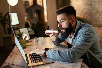 Young businessman using phone while working late on laptop in the office.