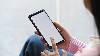 Mockup image of woman hands while holding black mobile phone with white blank screen .