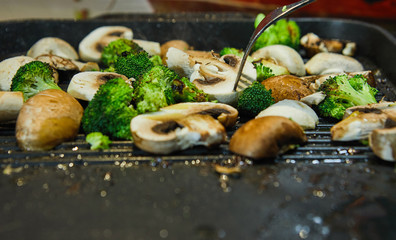 Fototapeta na wymiar Fresh champignon mushrooms and porcini mushrooms are fried on a board along with broccoli in butter. Healthy eating concept