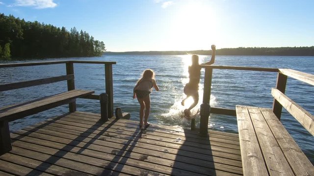 Family couple with daughter running on a wooden pier and jumping into the lake after the sauna in summer white night in Finland.